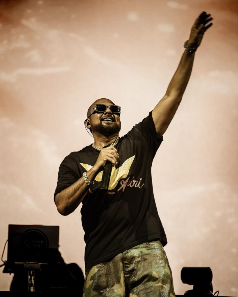 Sean Paul raising his hand and smiling on a gold background during his live performance at Kozel Carroponte, Milan, 2026